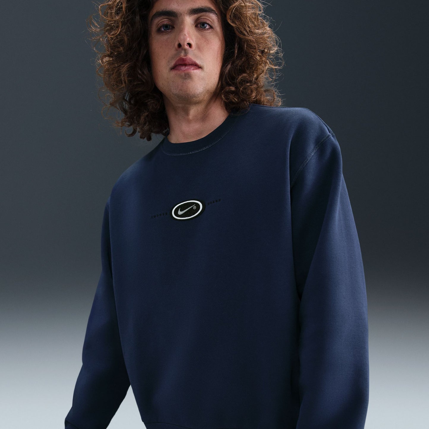 Person wearing a navy blue sweatshirt with a logo on a gradient background
