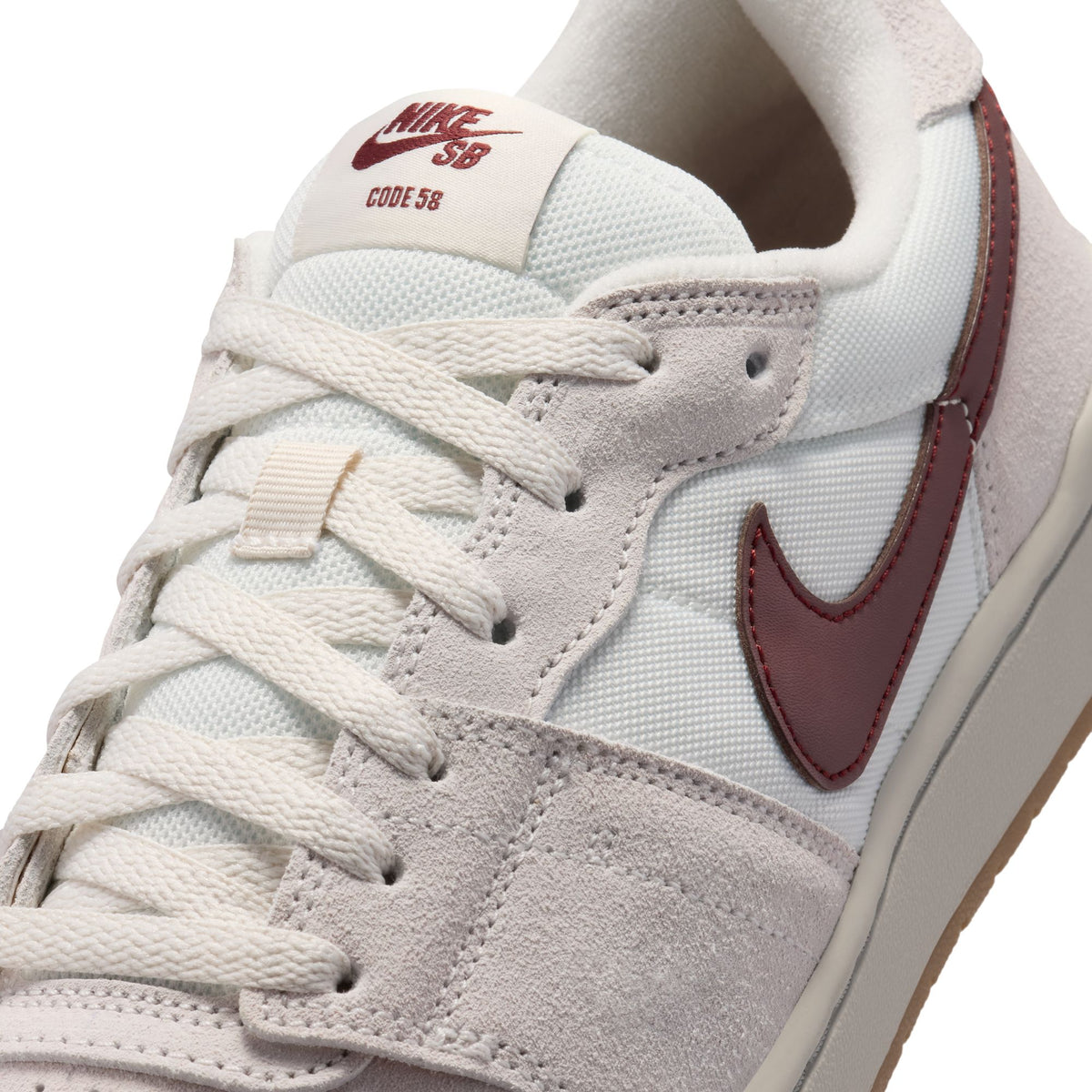 Close-up of a Nike SB Code 58 sneaker in off-white suede and canvas with a burgundy Swoosh and matching burgundy embroidery on the tongue.