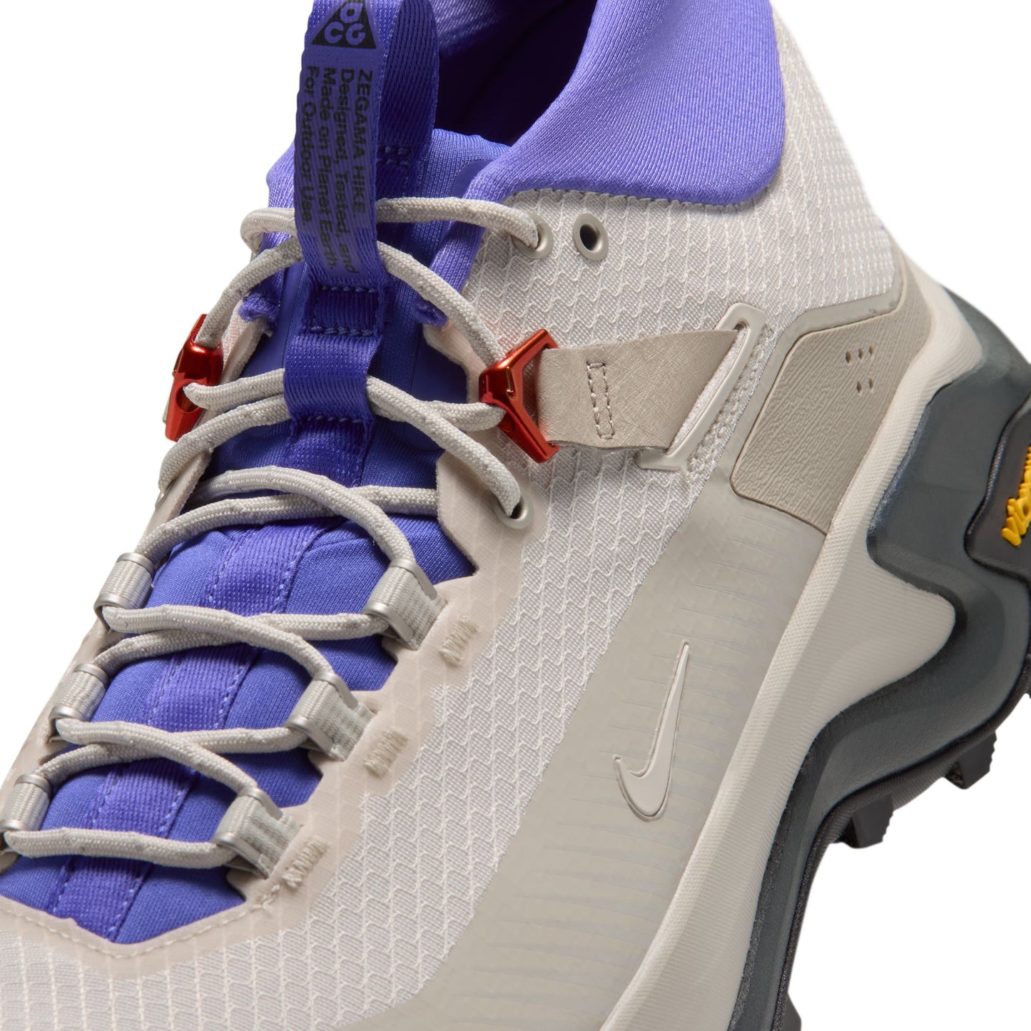 A close-up of a Nike hiking shoe in white and purple, featuring a white mesh upper, purple laces and collar, a beige strap, and a dark gray outsole.