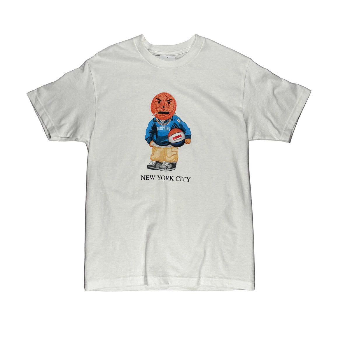 A white short-sleeve t-shirt laid flat on a white surface, featuring a cartoon graphic of a basketball character in a blue sweater and tan pants holding a basketball, with 'NEW YORK CITY' printed below.