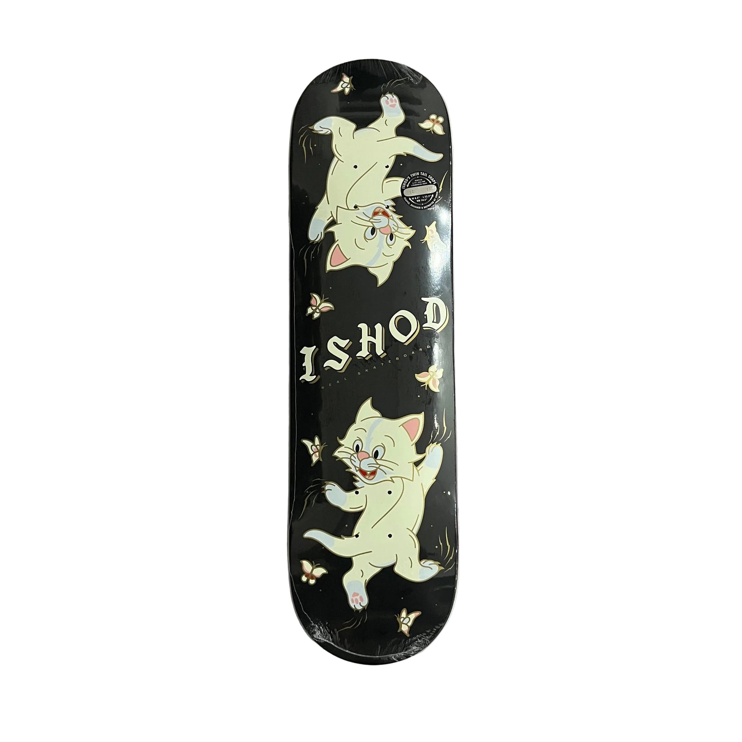 A skateboard deck featuring a black background with two cartoon kittens and the text 'ISHOD', photographed from above on a white surface.