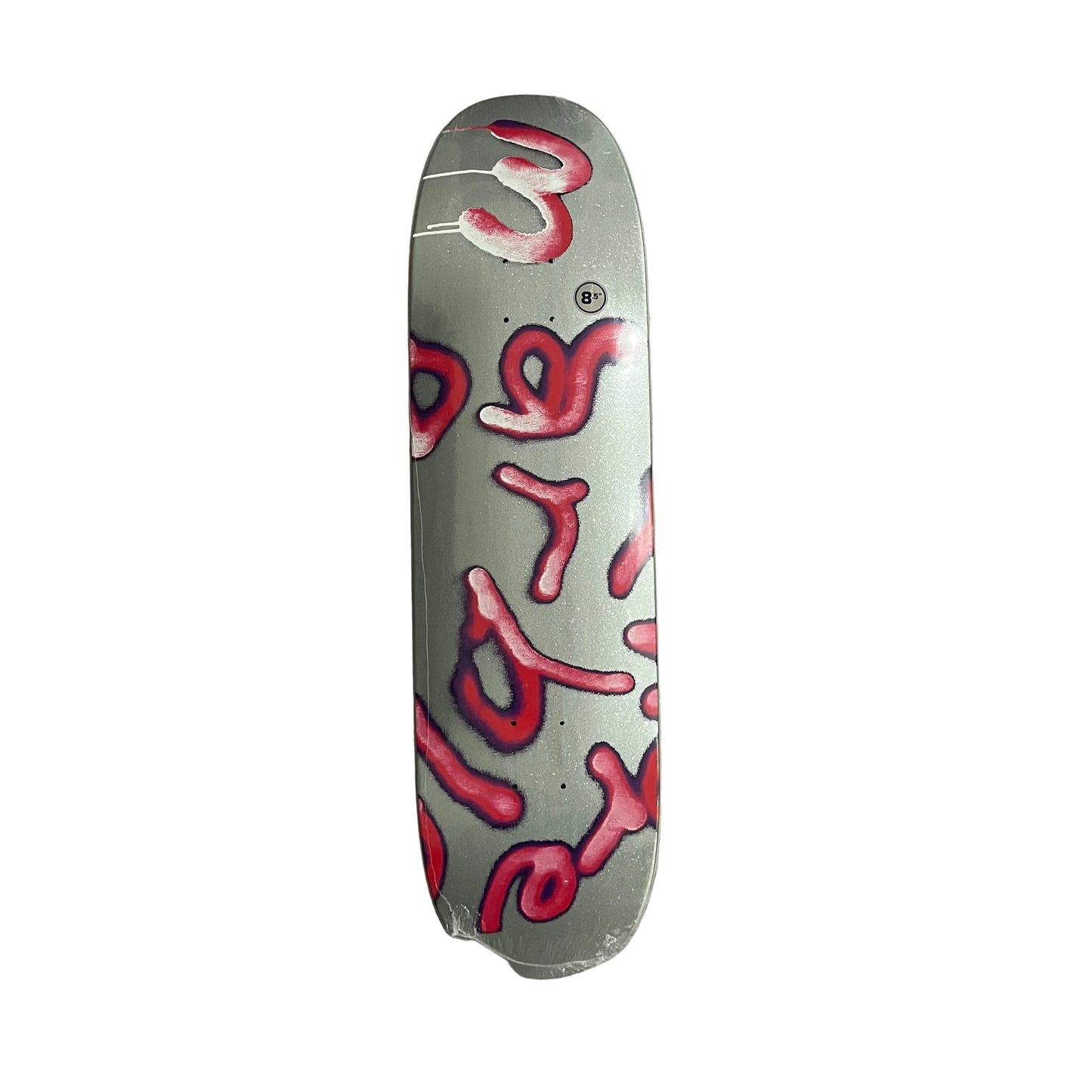 A skateboard deck with a metallic silver background and abstract red and pink graffiti-style lettering, photographed from above on a white surface.