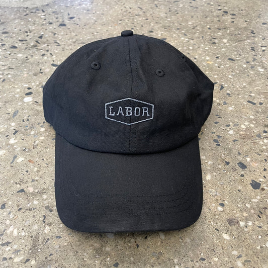 Front view of waxed canvas six panel cap with grey labor crest logo in center of cap