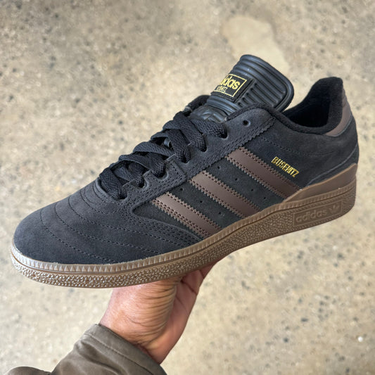 black suede sneaker with brown stripes, gum sole, and gold logo, side view