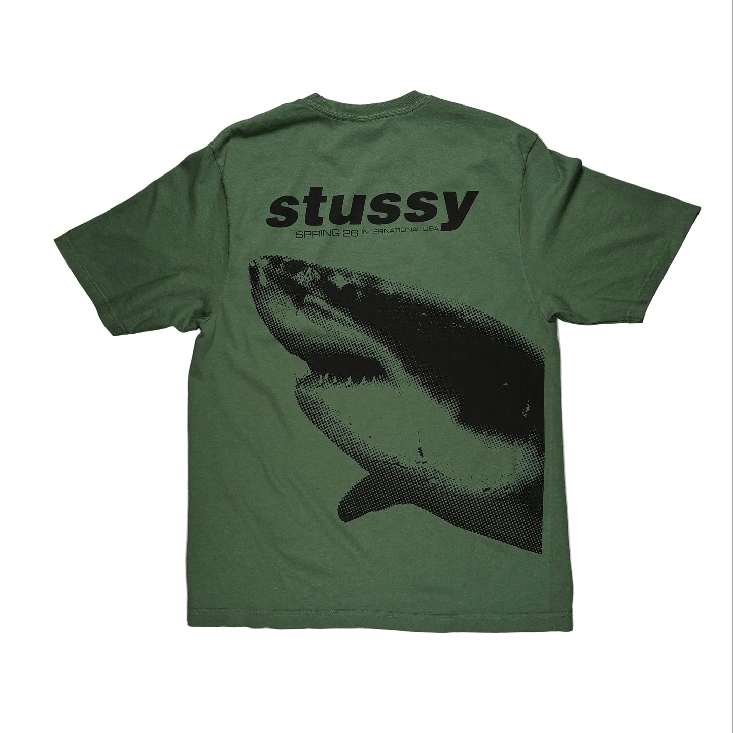 Green t-shirt with shark graphic and 'Stussy' branding on a white surface.
