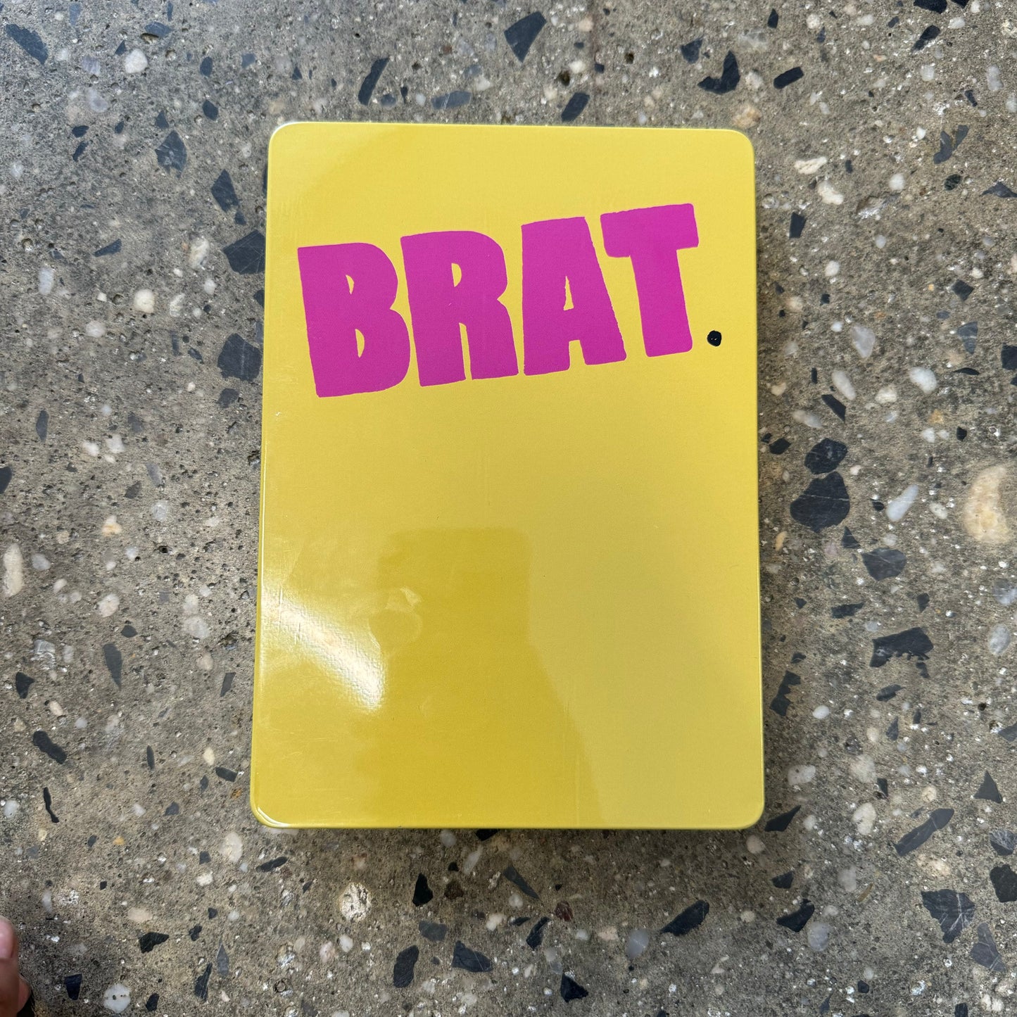 Front view of BRAT DVD case, pink logo on yellow metal case