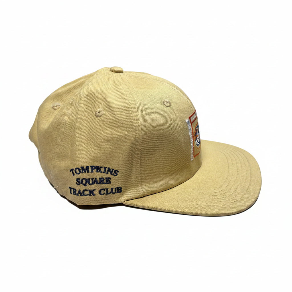 Beige cap with 'Tompkins Square Track Club' text on a white surface