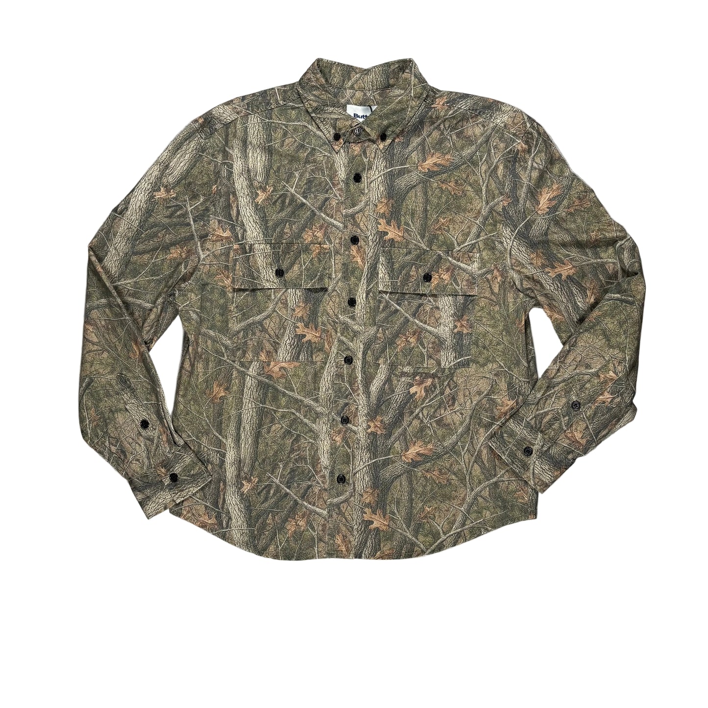 A long-sleeve button-up shirt with a woodland camouflage pattern, black buttons, laid flat on a white surface.