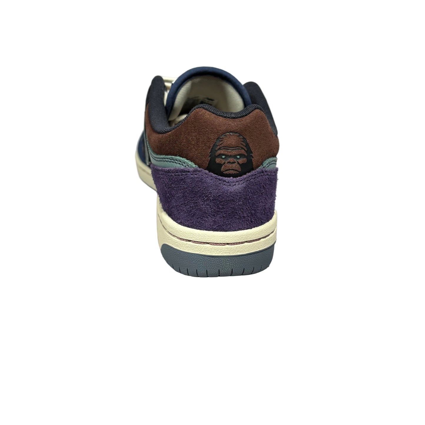 A single low-top sneaker shown from the back, featuring brown suede, purple suede, navy overlays, and a small gorilla face graphic on the heel. The shoe is photographed on a white background.