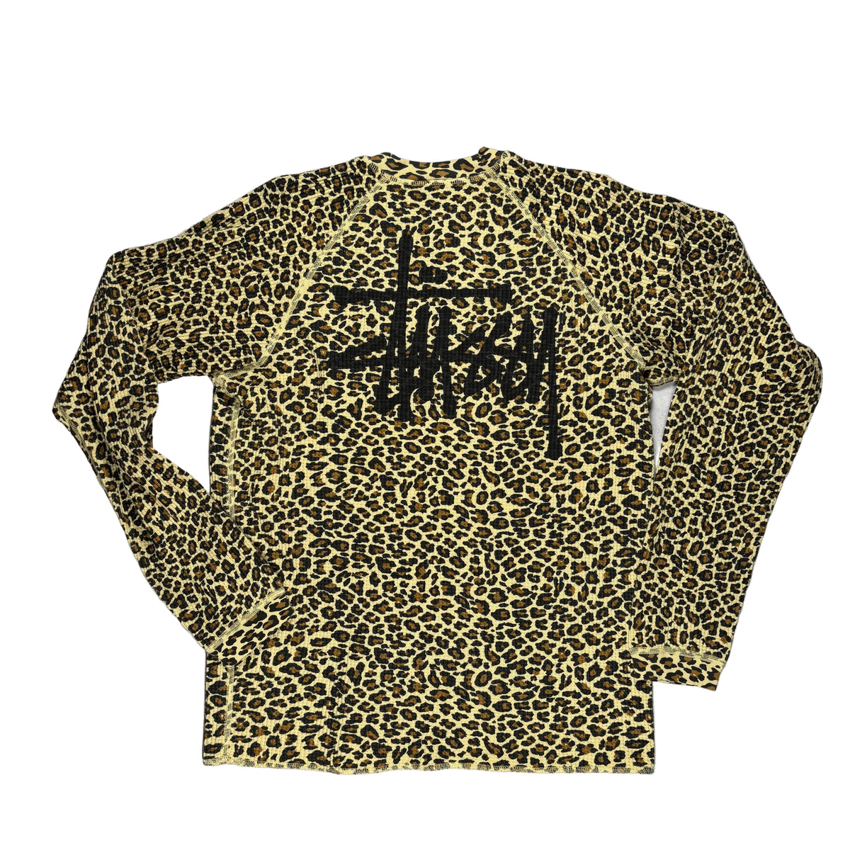 Back view of a long-sleeve crewneck shirt featuring a classic leopard print pattern in tan and black, with a large black Stussy logo printed across the back, laid flat on a white background.