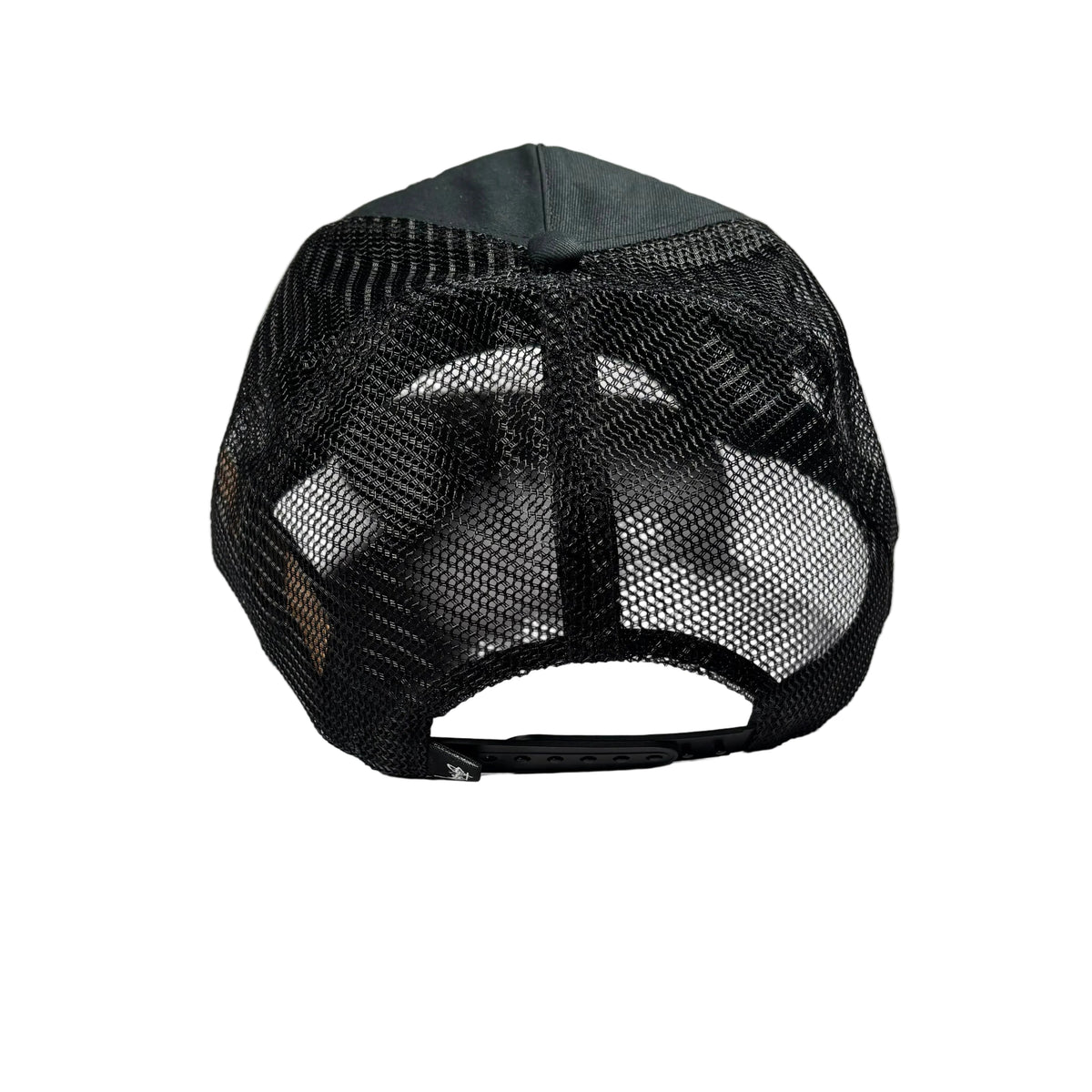 A black trucker-style baseball cap viewed from the back, featuring a black mesh back and a black fabric crown, resting on a white surface.
