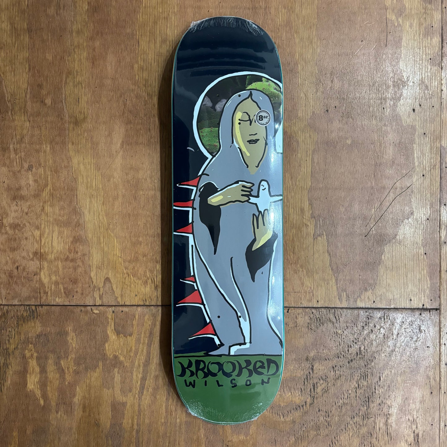 view of black, grey, green and red skateboard deck with grey figure holding a SHMOO figurine