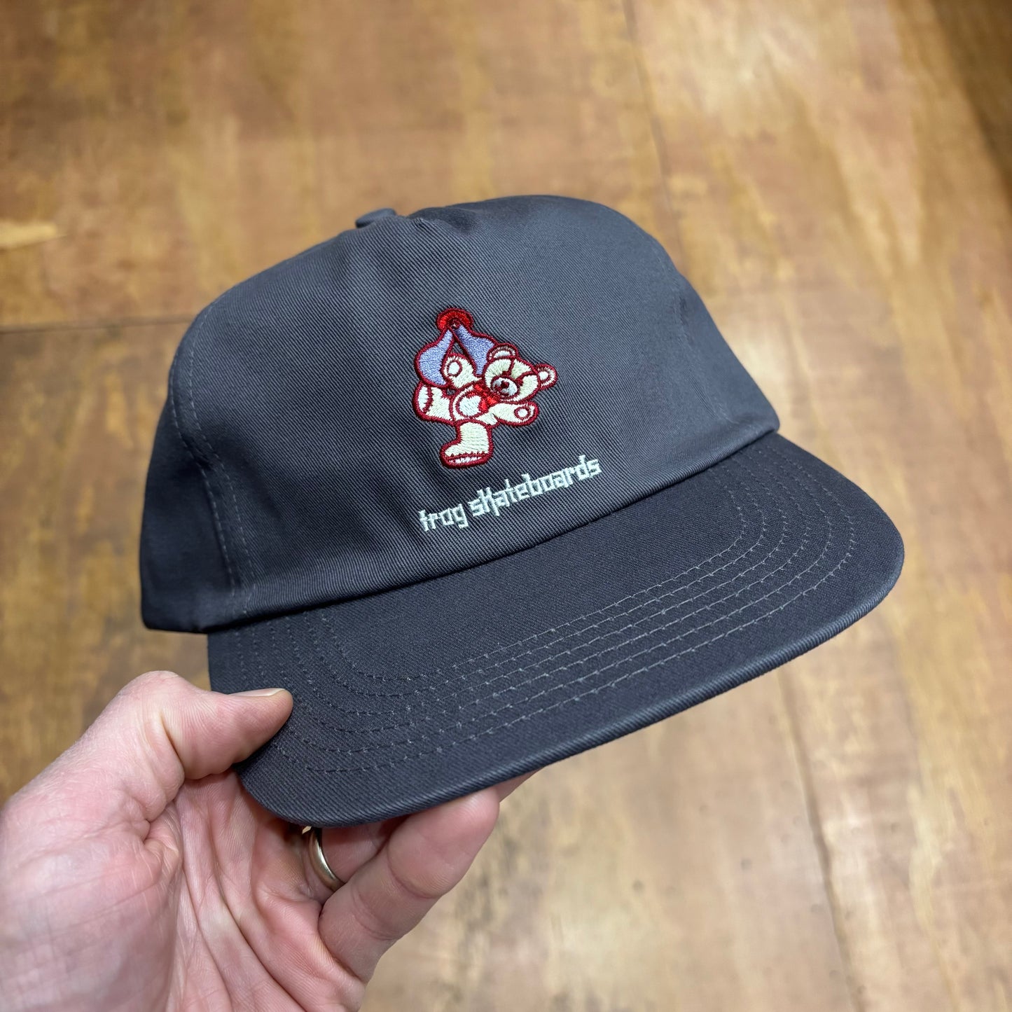 front view of grey cap with teddy bear in claw of claw machine game