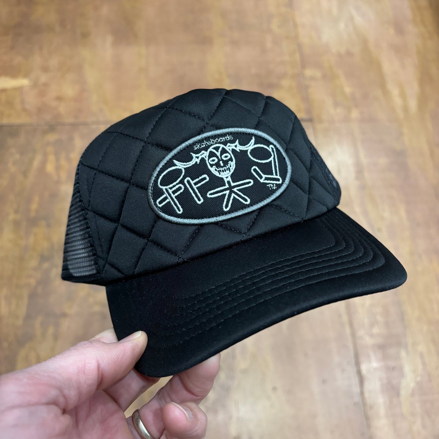 Front view of all black mesh trucker cap with oval FROG patch in middle