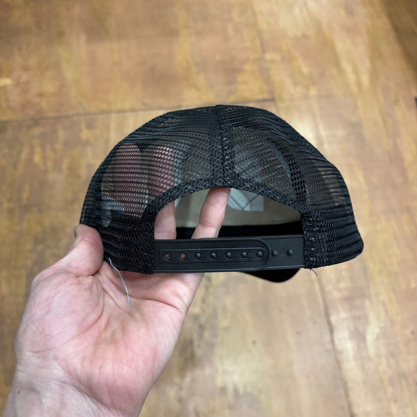 rear view of all black mesh trucker hat back, with snap closure