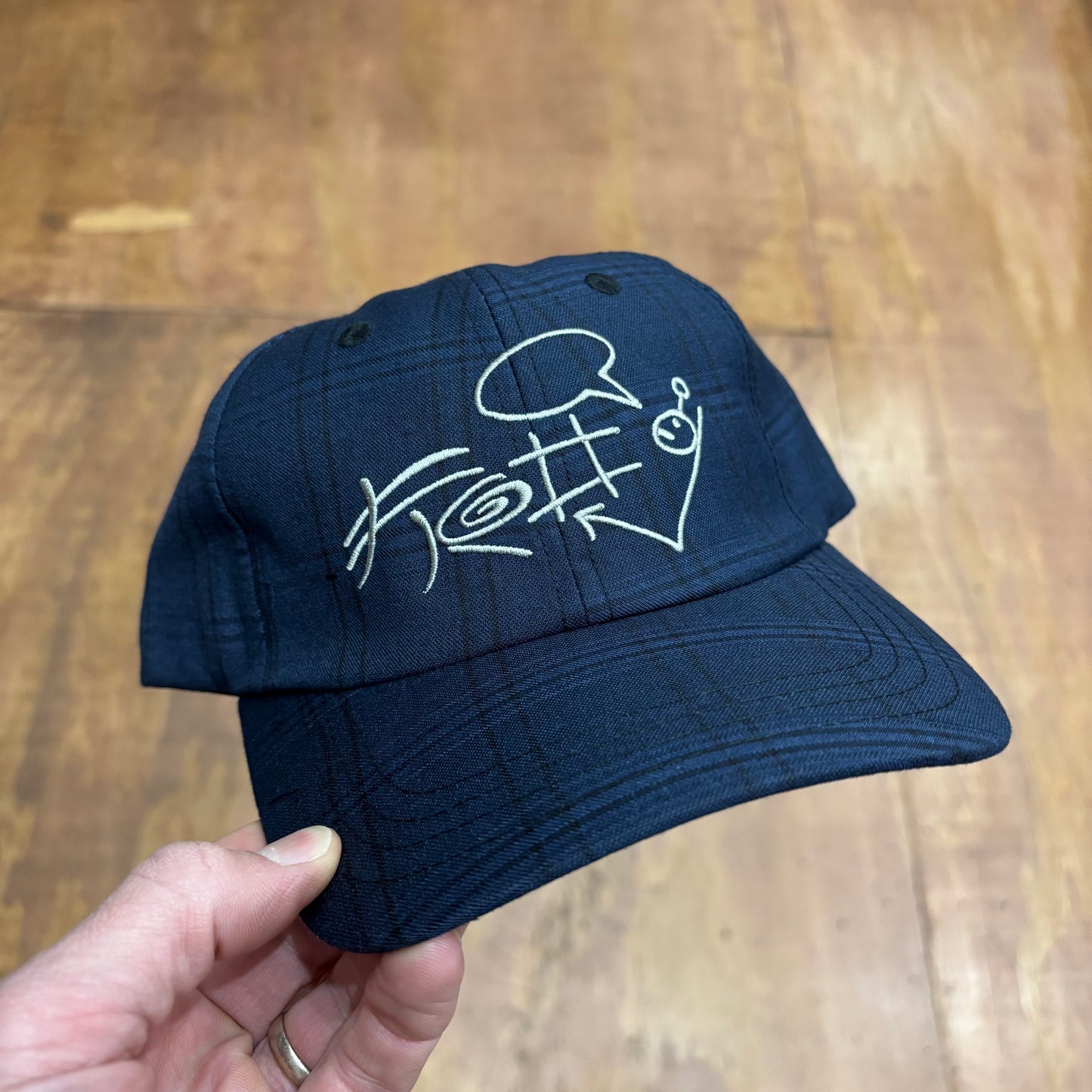 front view of navy plaid hat with crudely drawn FROG logo on front of cap