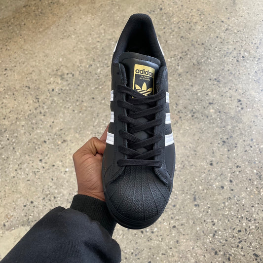 black leather sneaker with white stripes and gold logo, top view