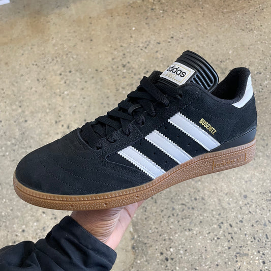 black suede sneaker with white stripes, gum sole, and gold logo