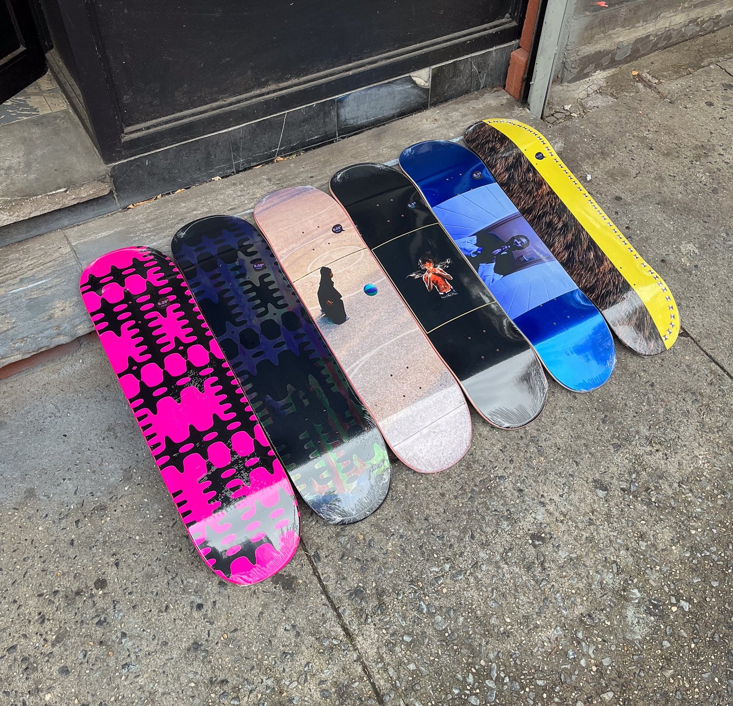 Violet Brand skateboard decks in blue, black, yellow and purple with assorted colored picture graphics in the middle of each one