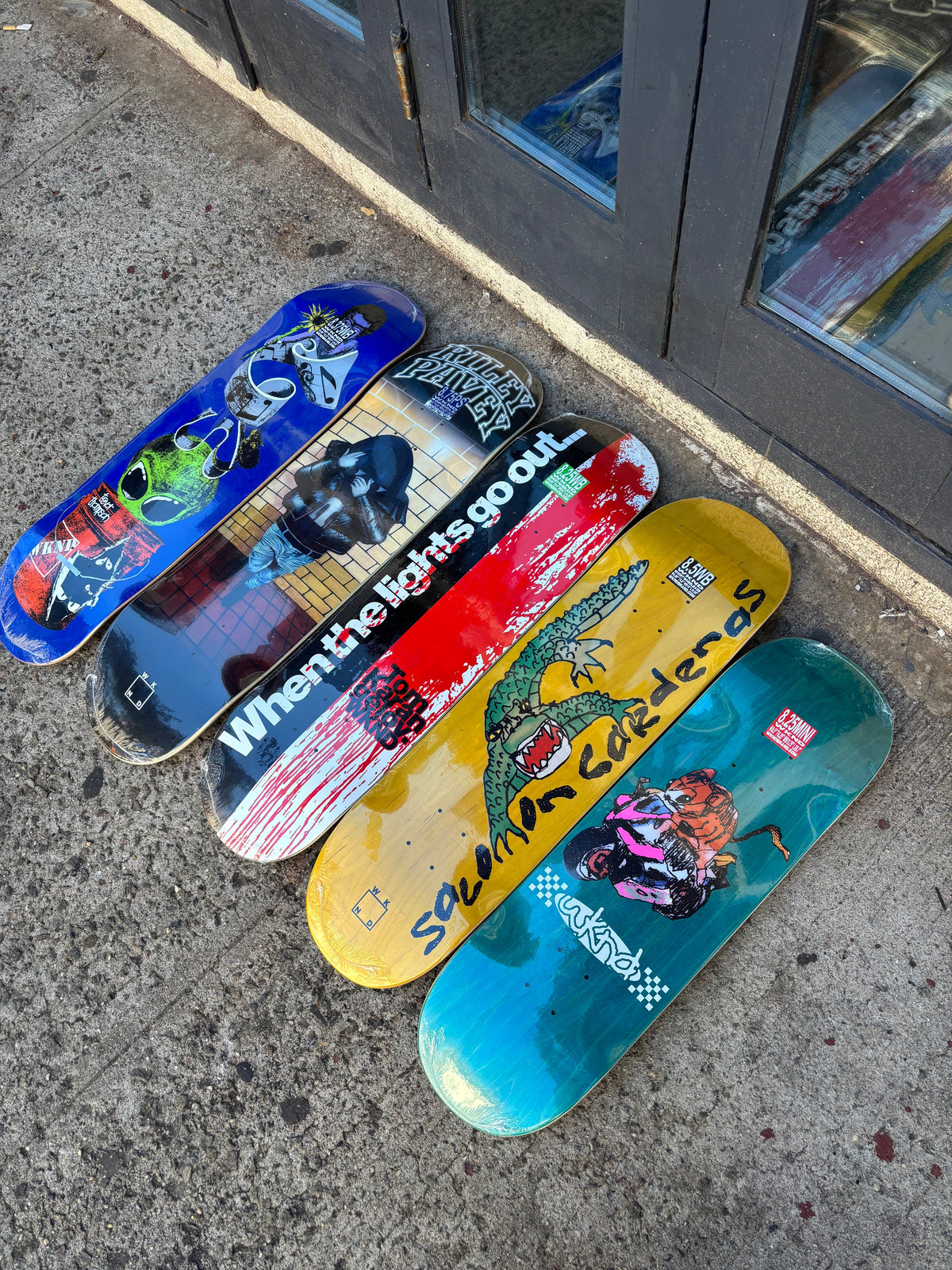 five vibrant colored skateboard decks laid on a sidewalk