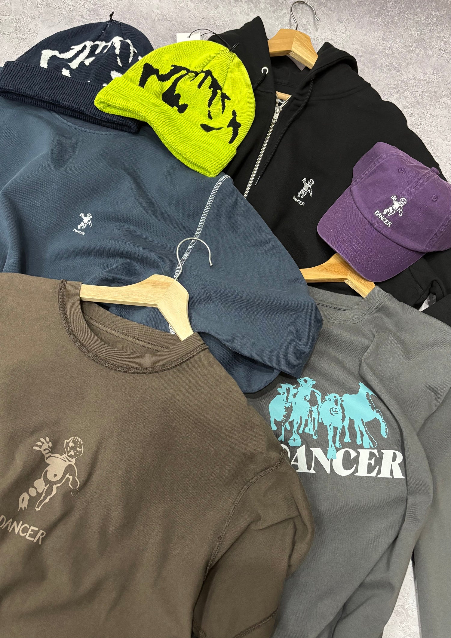 assorted dancer tees, sweatshirts, beanies and hats against a grey background