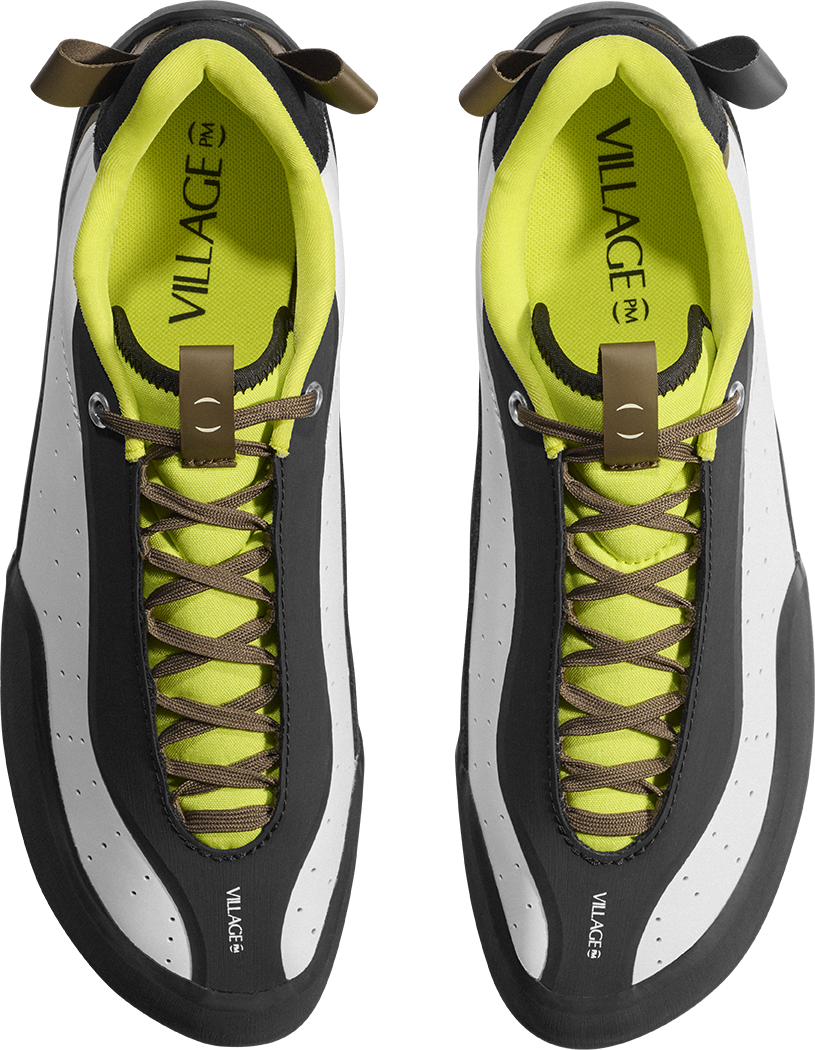 A pair of VILLAGE brand low-top sneakers shown from a top-down view. The shoes feature a black and white leather upper with a vibrant neon yellow-green lining and matching laces, accented by brown leather pull tabs.
