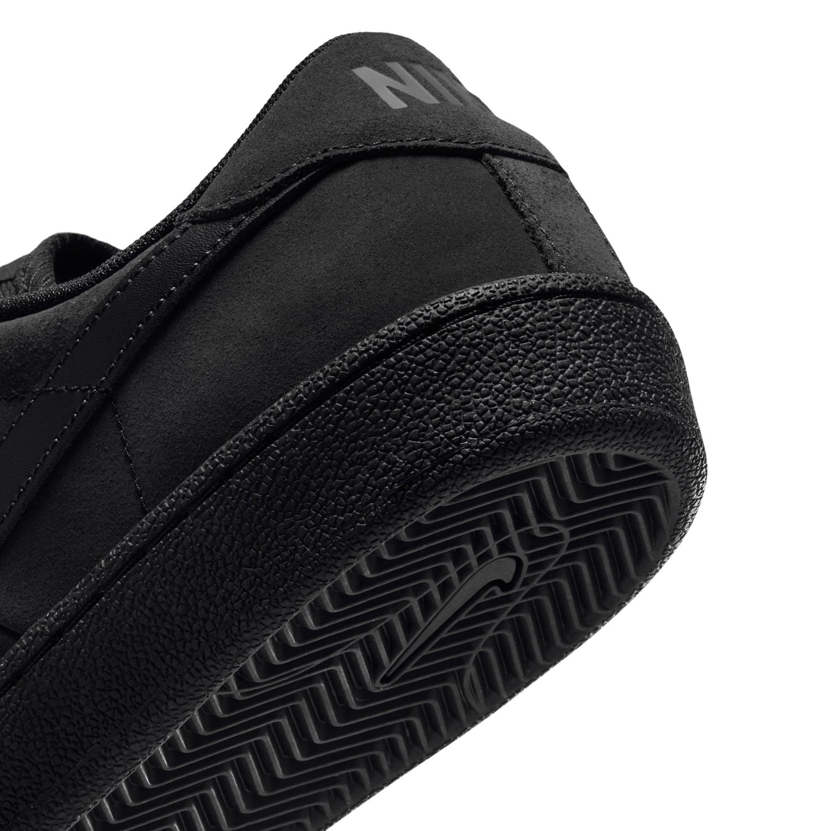 Close-up of a black Nike sneaker showing the heel, textured leather upper, and patterned rubber outsole on a white background.