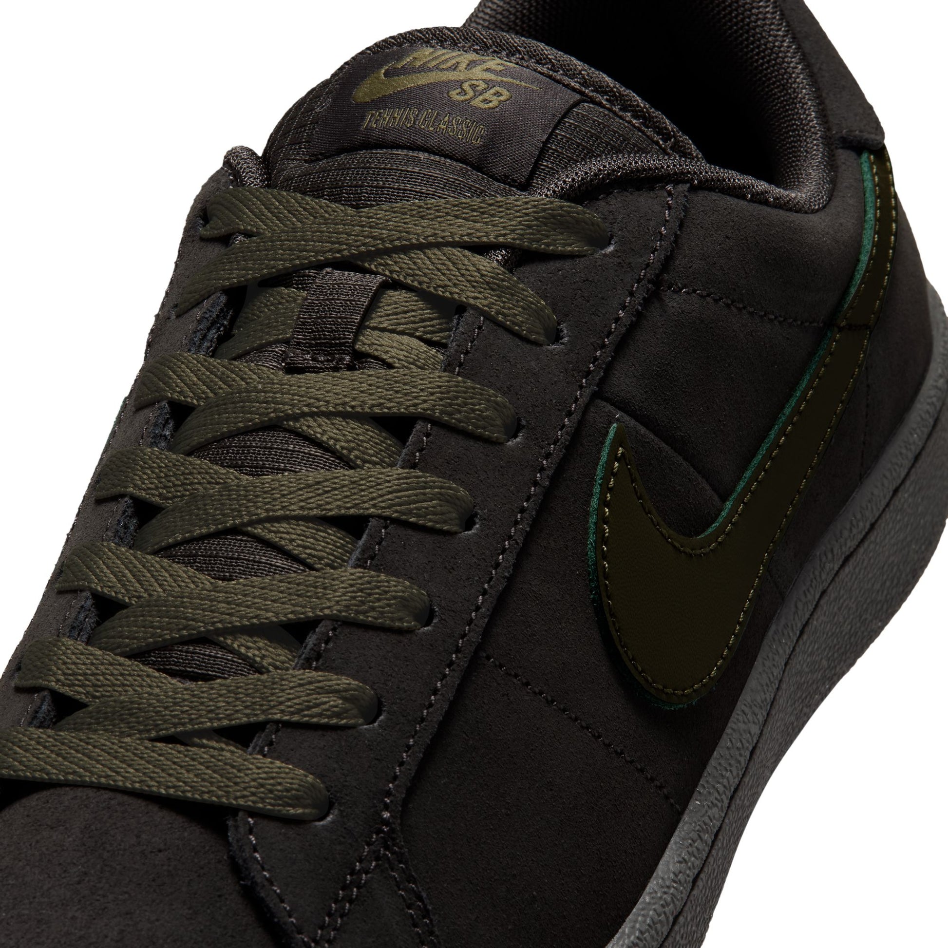 Close-up of a Nike SB skate shoe in black suede with olive green laces, a matching green Swoosh, and green stitching details on a white background.