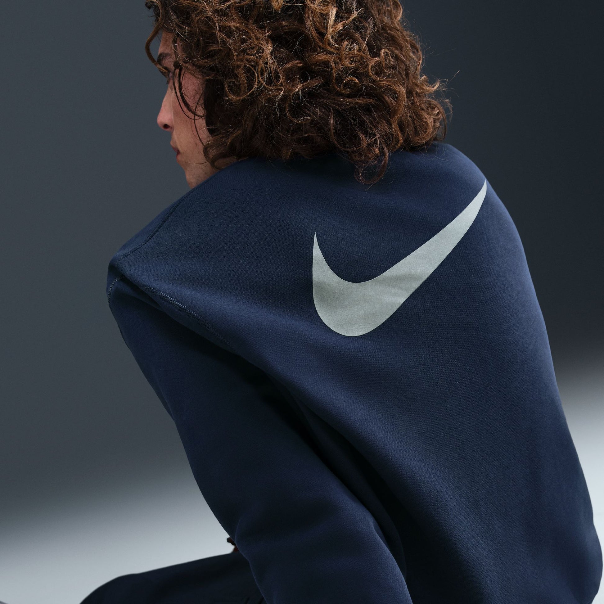 Person wearing a navy blue hoodie with a white logo on a gradient background