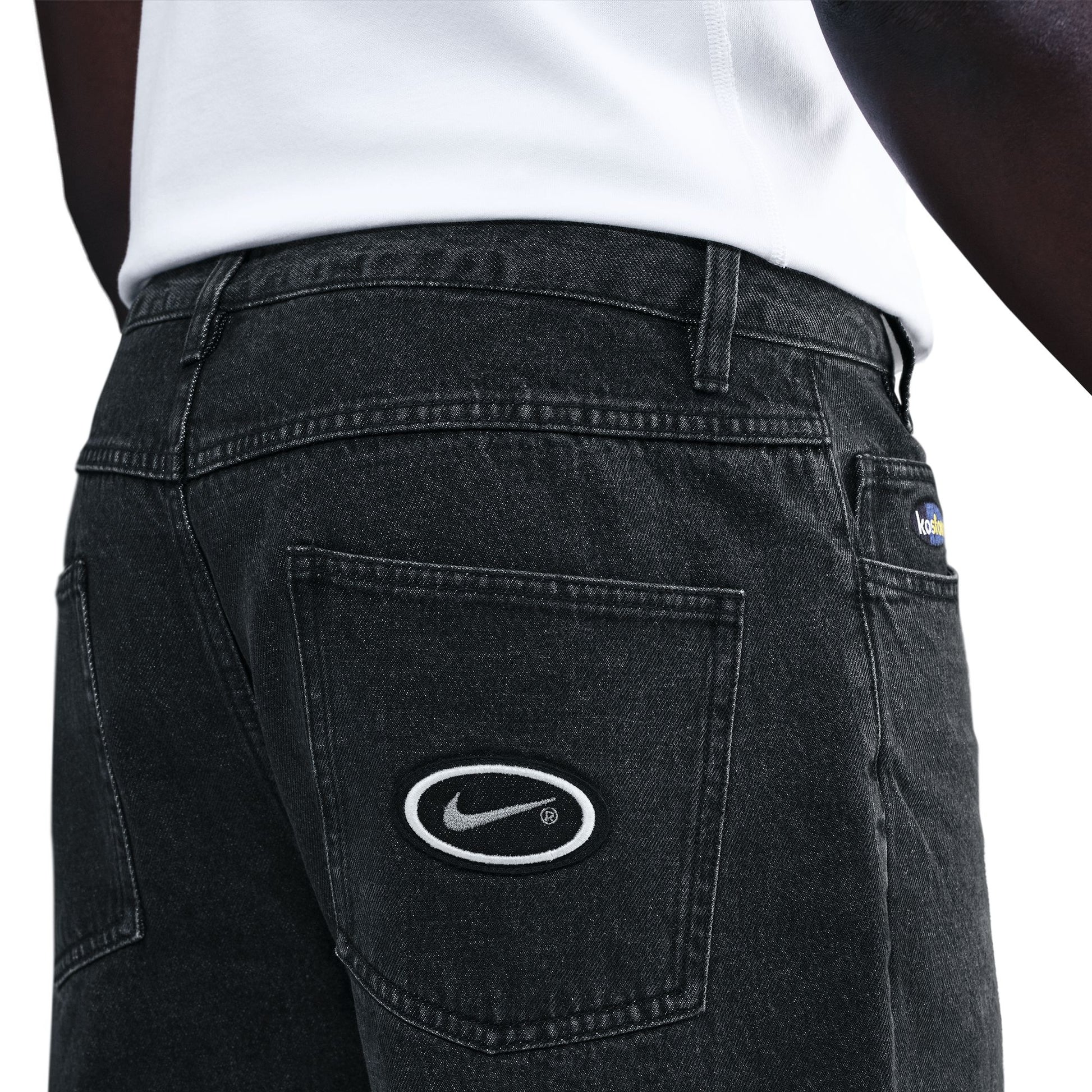 Black jeans with a Nike logo on the back pocket against a white background