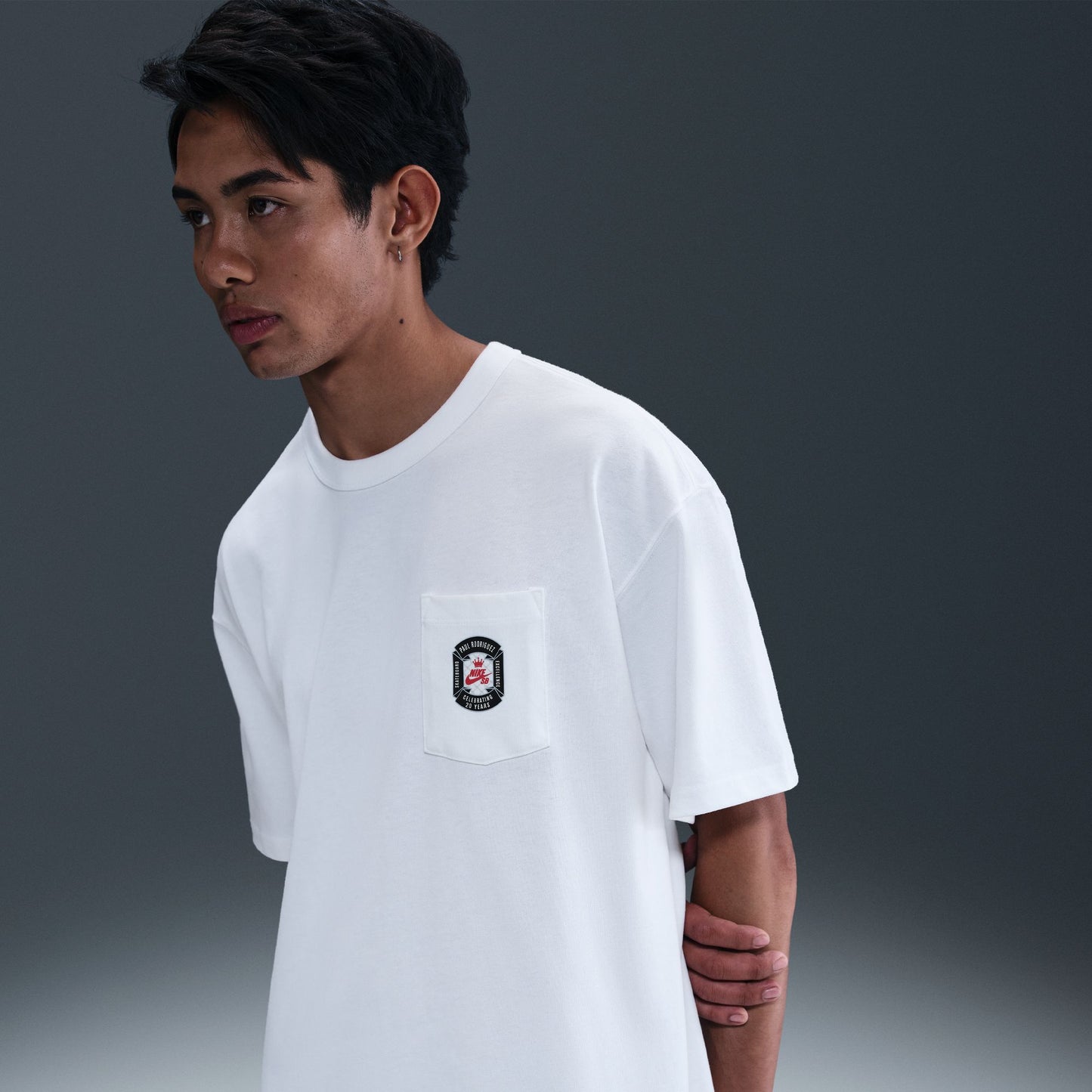 Person wearing a white t-shirt with a small logo on a gradient gray background