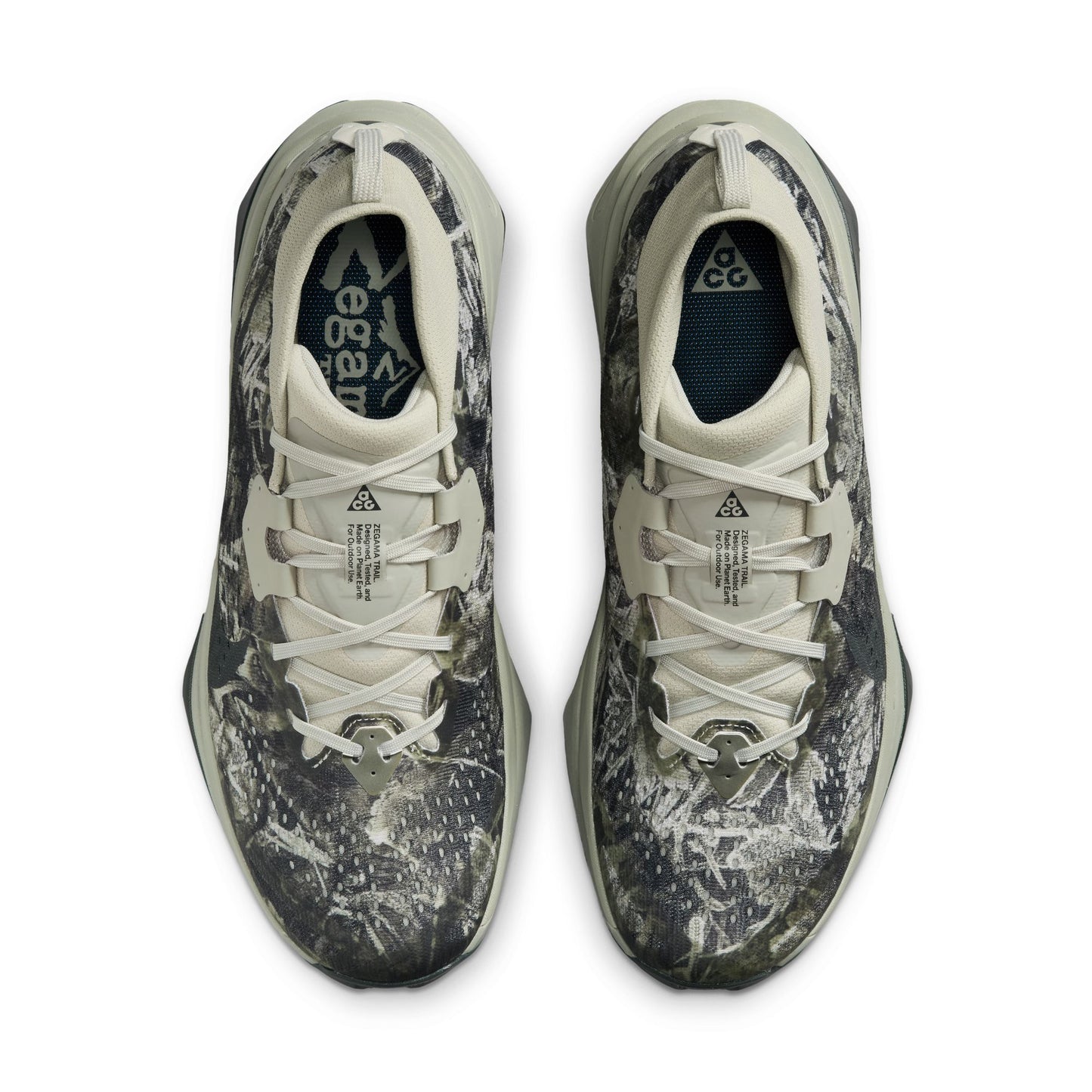 A pair of Nike zegama trail sneakers shown from a top-down view. The shoes feature a dark gray and black abstract camo pattern on a light gray and off-white base, with white laces