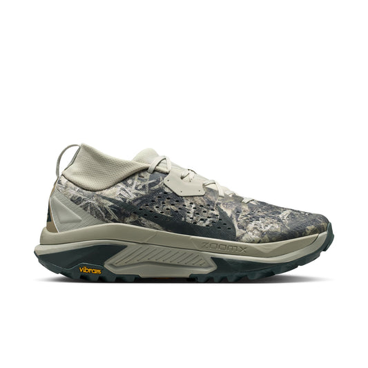 A single running shoe shown in profile against a solid white background. The shoe features a camouflage pattern upper in shades of gray, beige, and brown, with a light beige midsole and a dark gray Vibram outsole.