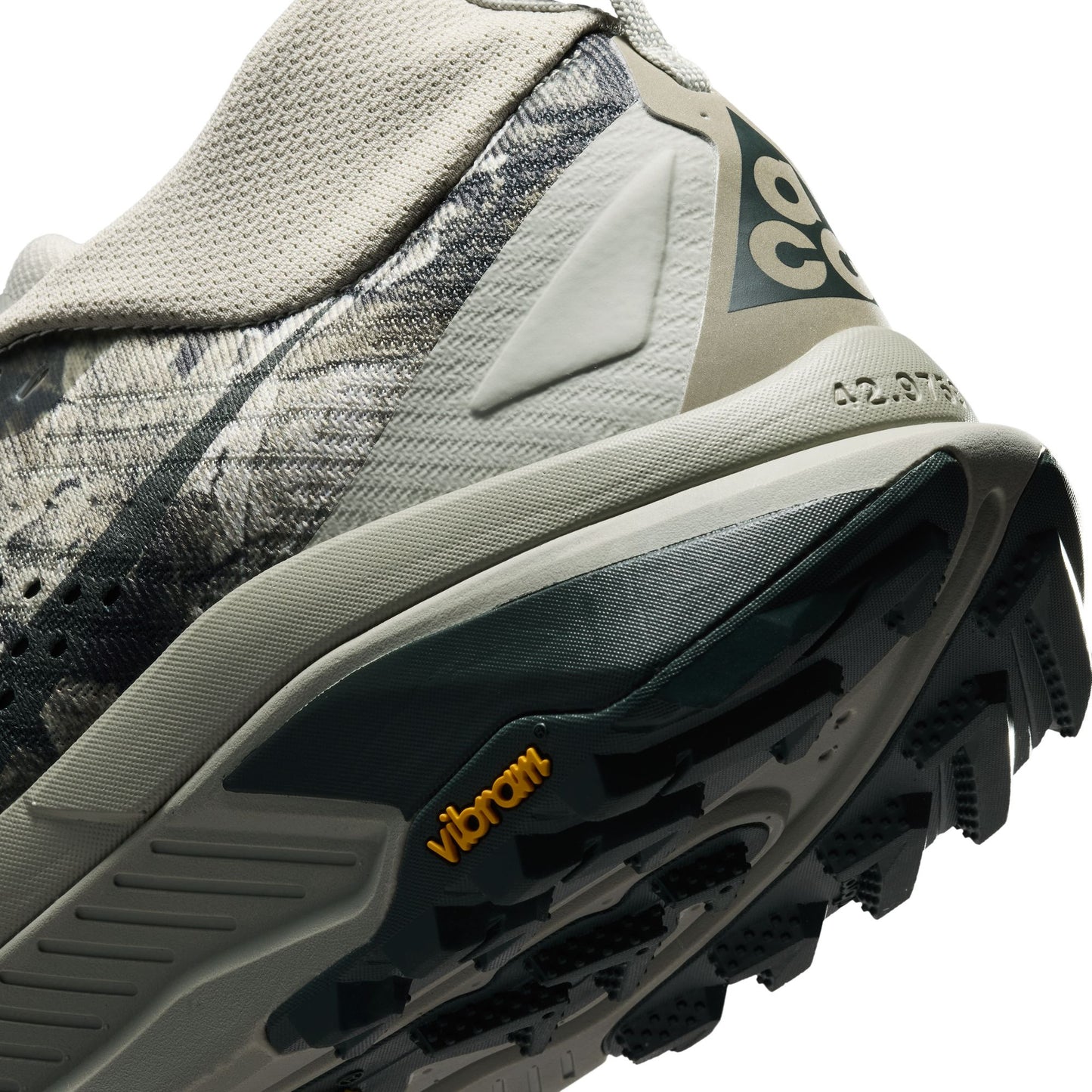 Close-up of a trail running shoe showing the midsole, outsole, heel counter, and part of the upper in gray, black, and beige tones with a visible Vibram logo.