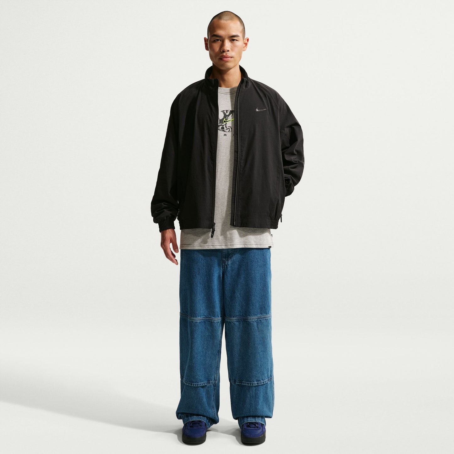 Man wearing a black jacket, gray shirt, and blue jeans on a white background