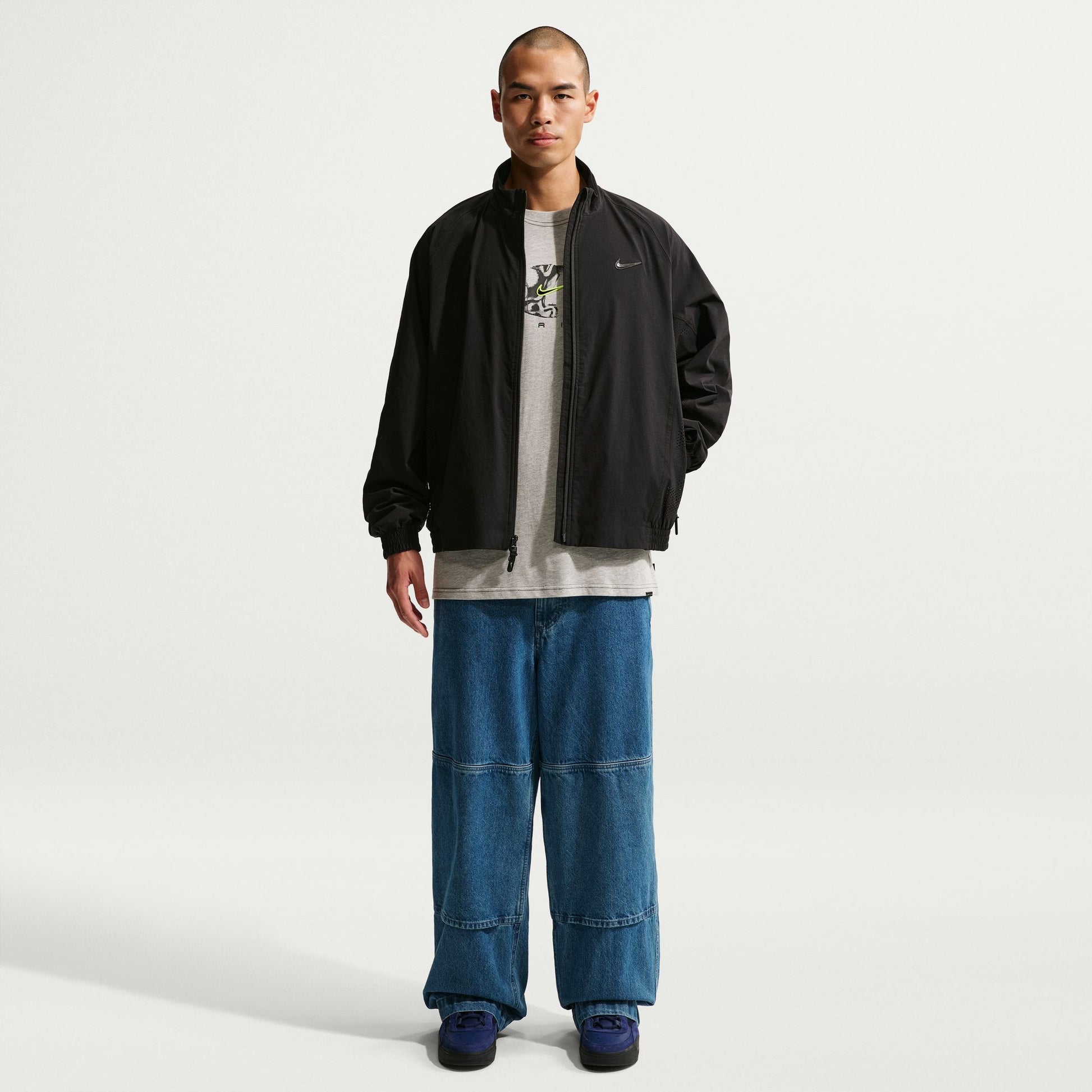 Man wearing a black jacket, gray shirt, and blue jeans on a white background