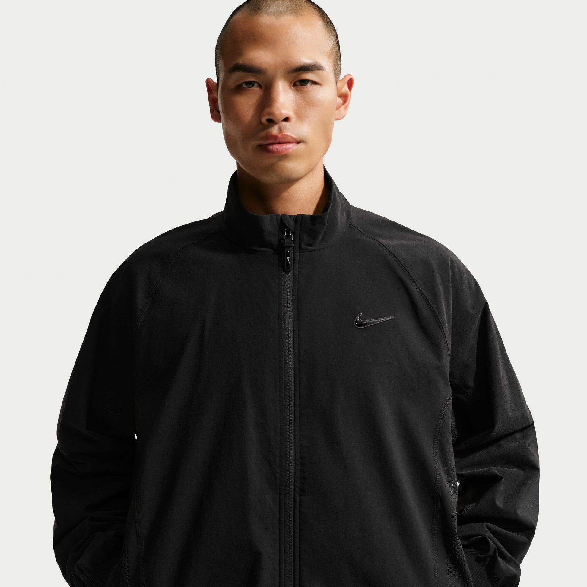 Man wearing a black jacket with a nike brand logo on a light gray background