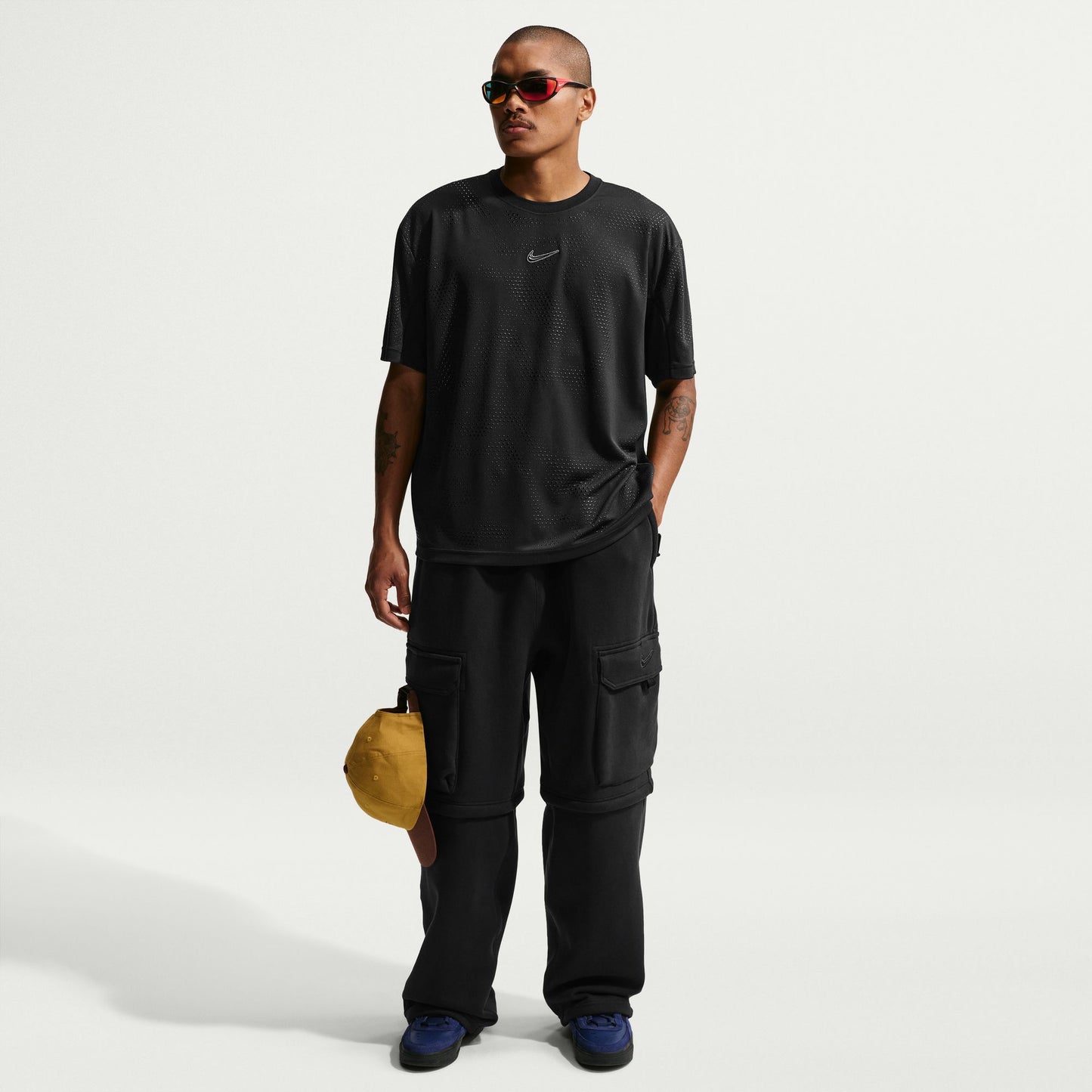 Man wearing a black t-shirt and cargo pants holding a yellow bag on a white background