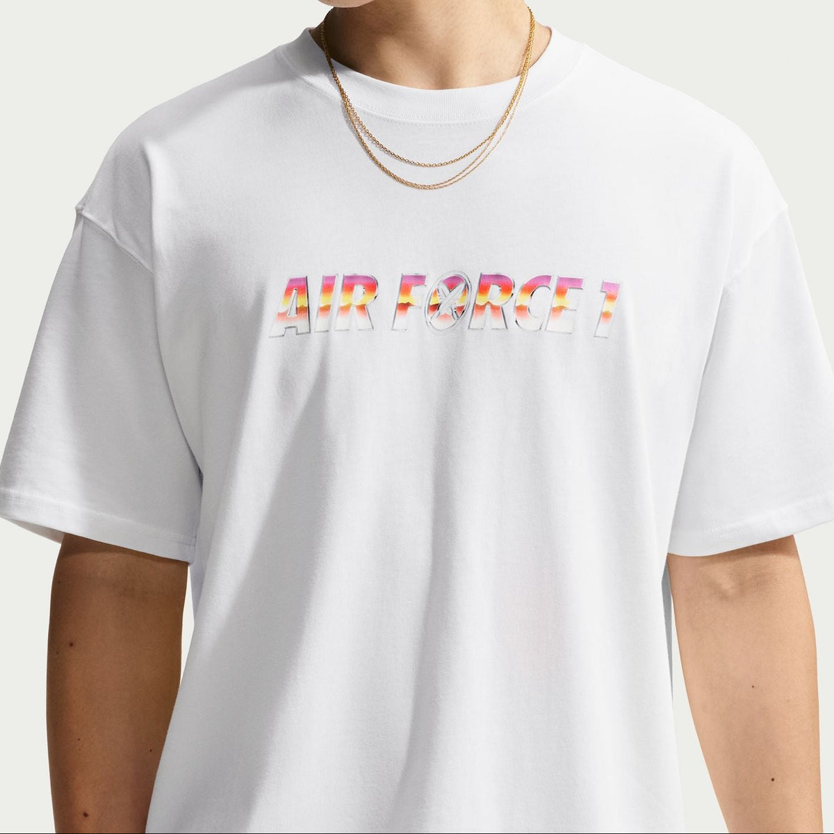 A model wearing a white oversized t-shirt with 'AIR FORCE' printed across the chest in a colorful, textured pattern, set against a plain light gray background.