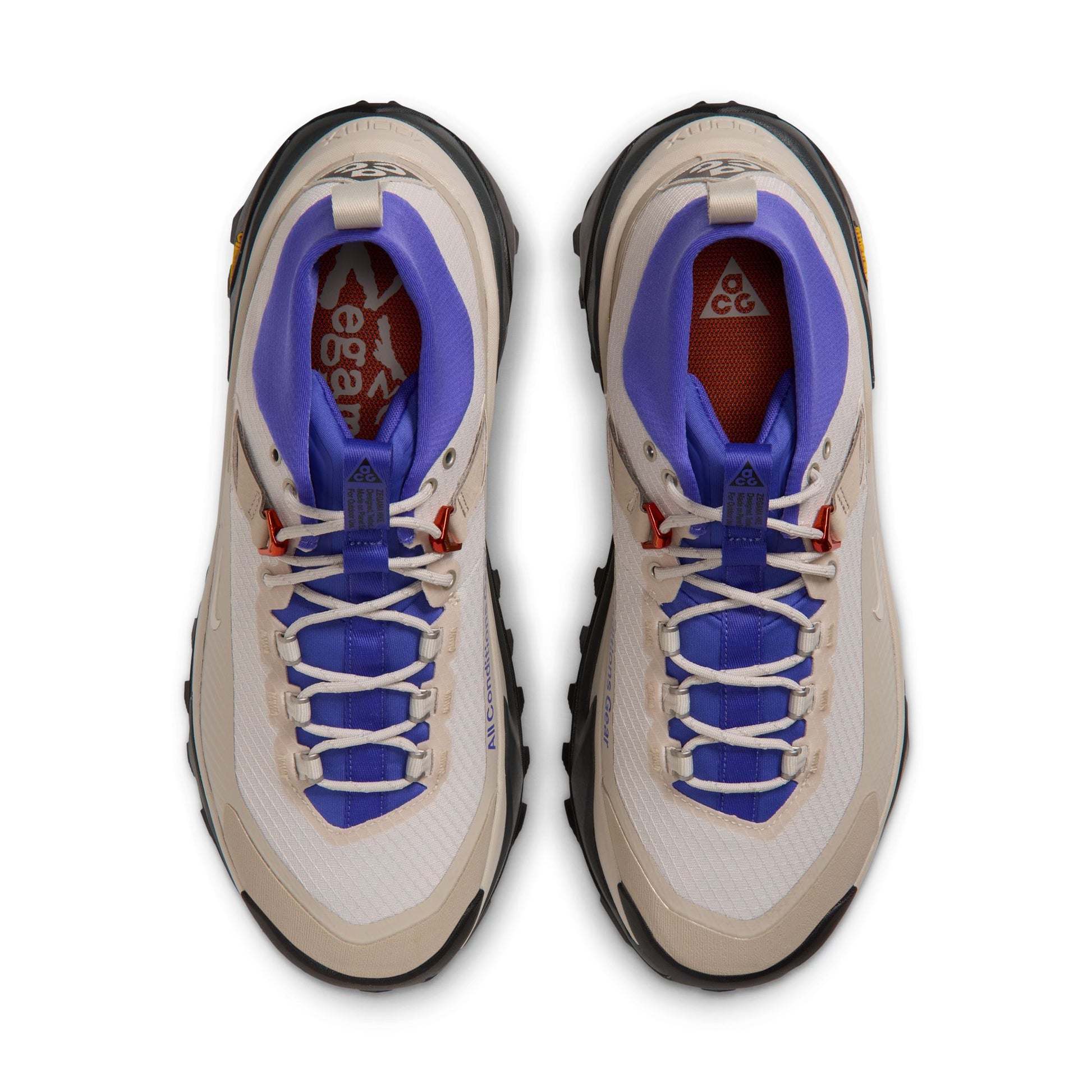 A pair of nike acg hiking shoes shown from a top-down view on a plain white background. The shoes feature a cream and white mesh upper with vibrant blue tounge and lining, a red interior collar, and black outsole detailing.