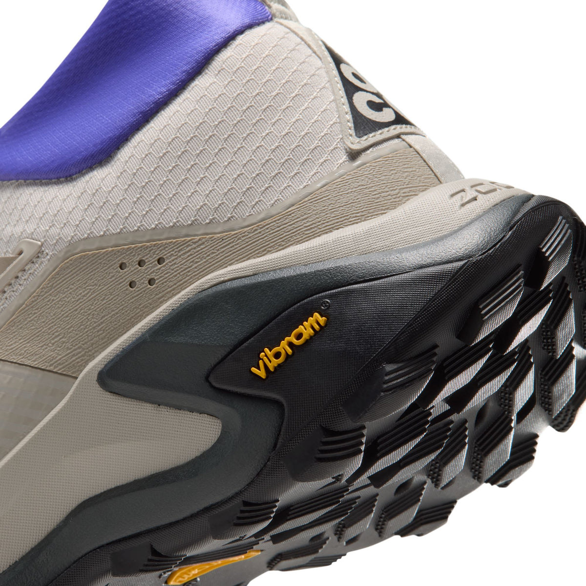 Close-up of a trail running shoe showing the side and sole, featuring a beige and gray mesh upper, a purple collar, and a black Vibram outsole with yellow logo accents.