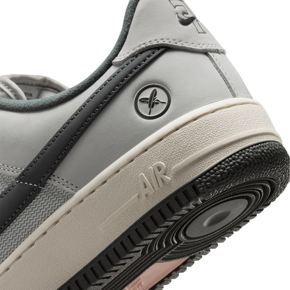 Close-up of the heel and midsole of a gray and black sneaker with a cream-colored midsole and a circular logo on the side.