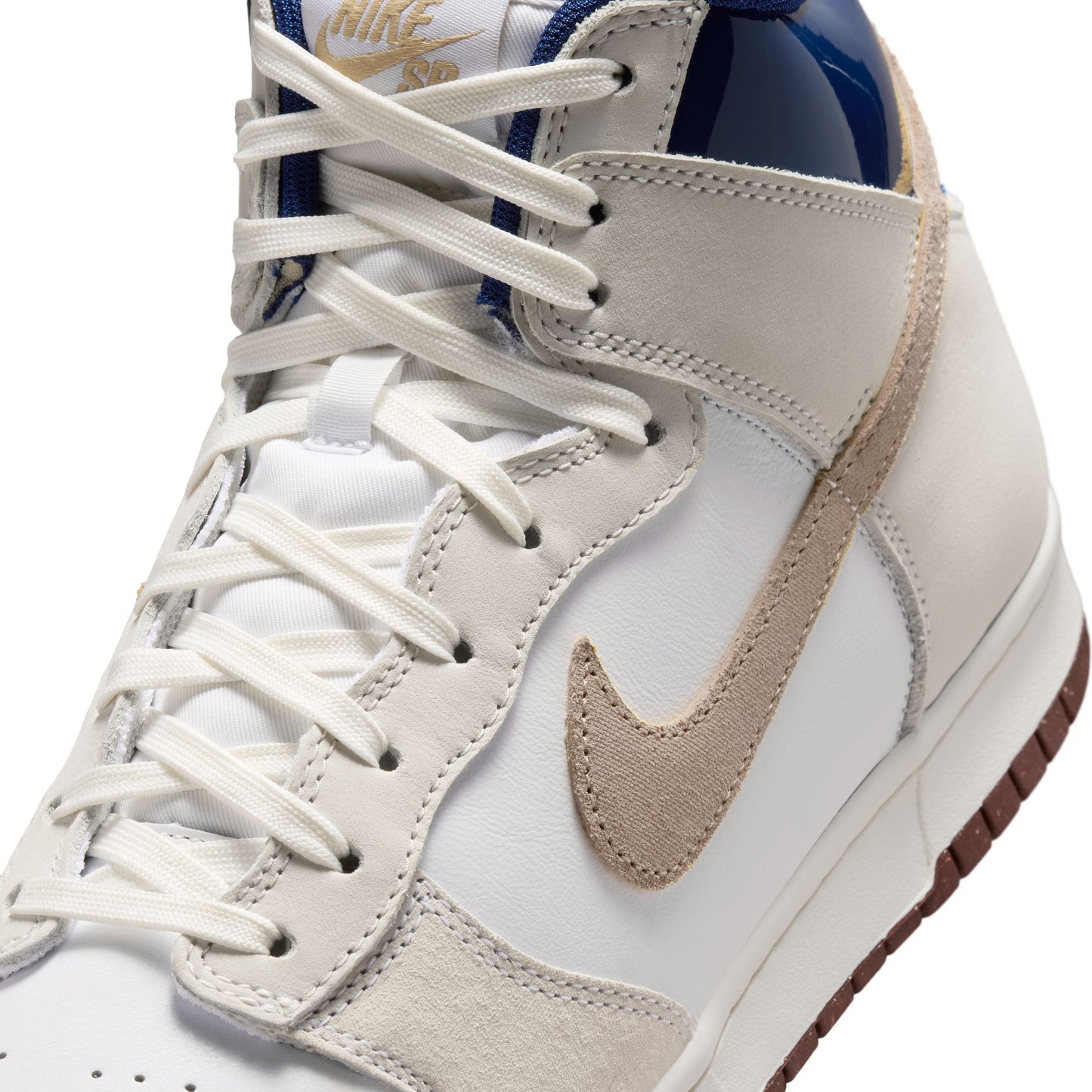 A close-up of a Nike high-top sneaker in white, beige, and navy blue, showing the side profile with white laces and a beige Swoosh.