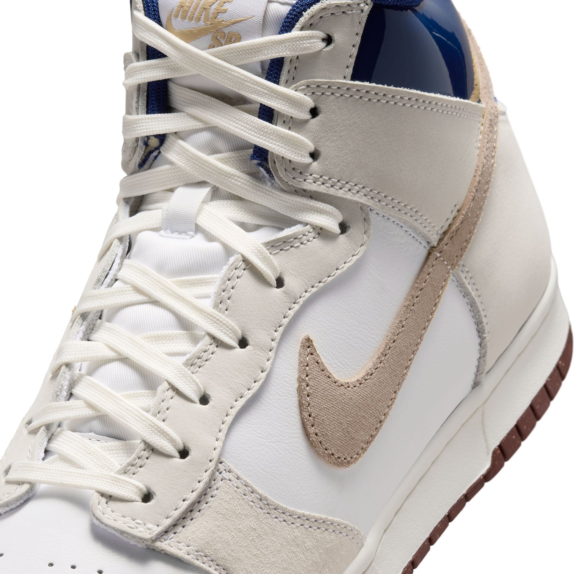 A close-up of a Nike high-top sneaker in white, beige, and navy blue, showing the side profile with white laces and a beige Swoosh.
