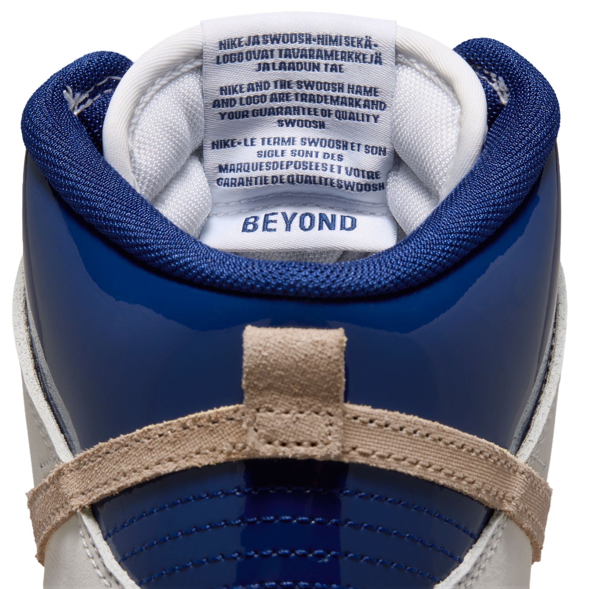 Close-up rear view of a Nike Beyond sneaker in navy blue, white, and beige, showing the collar, tongue with branding, and heel strap.