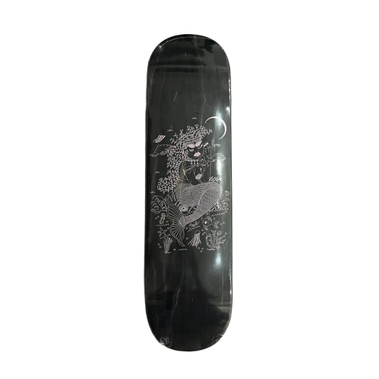 A black skateboard deck with a detailed white and gray illustration of a mermaid under a crescent moon, resting on a white surface.