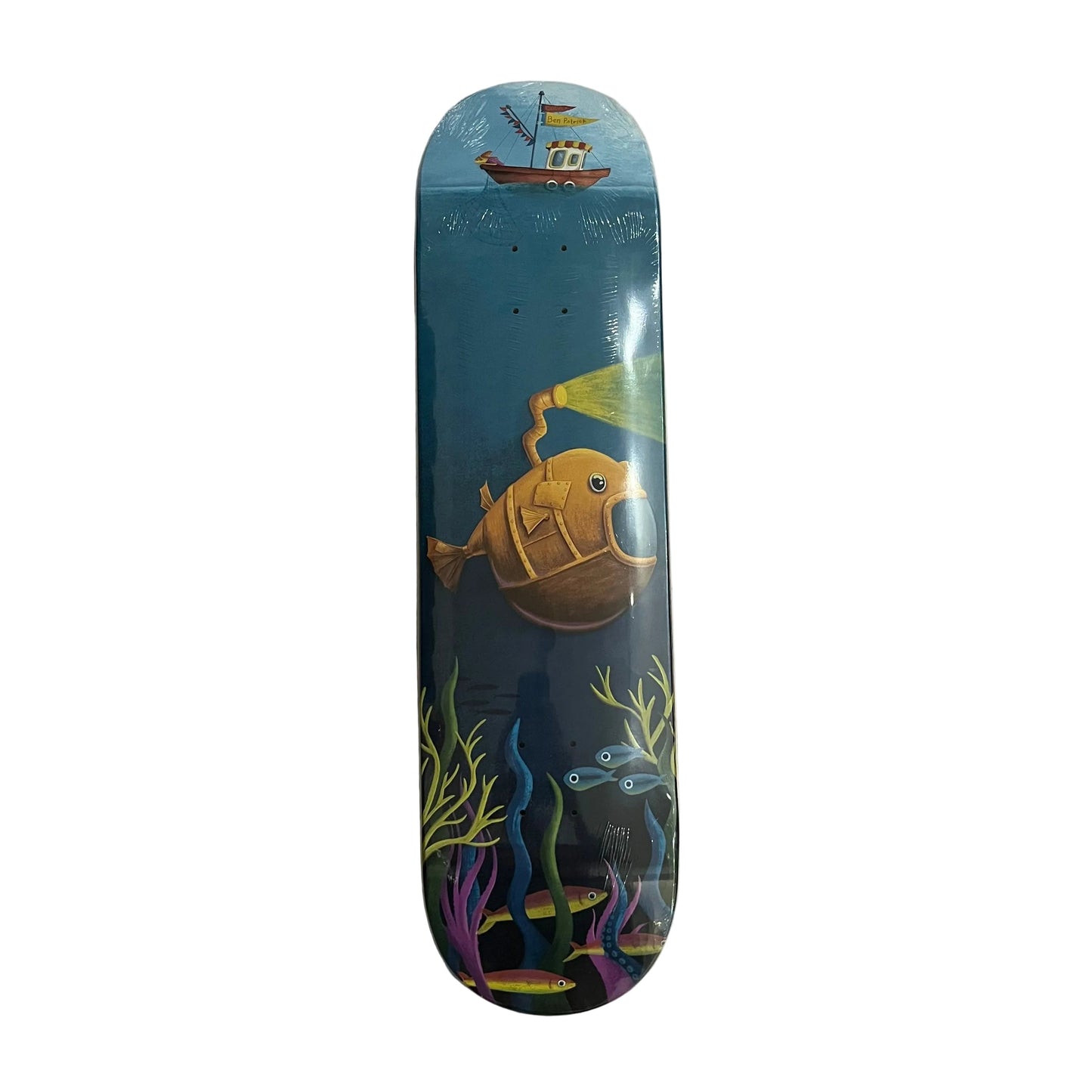 A skateboard deck with a colorful underwater graphic design, featuring a yellow submarine, blue ocean, and sea plants, photographed flat on a white surface