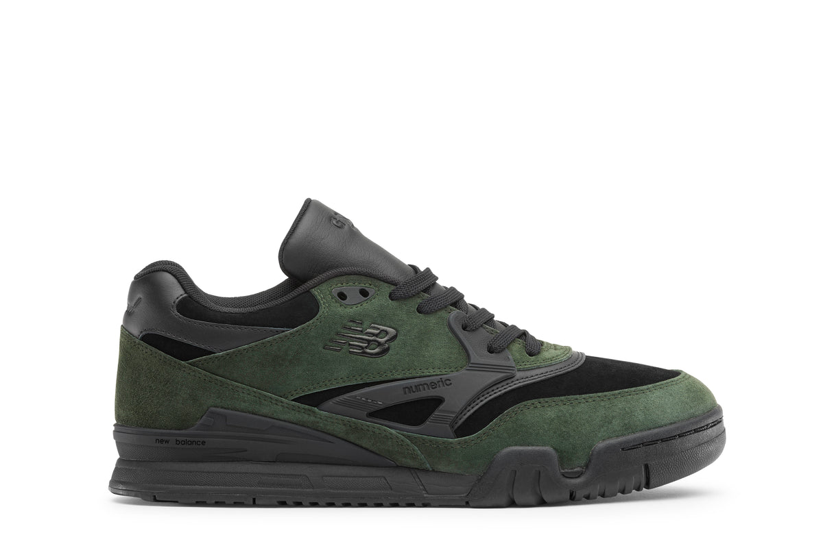 A New Balance low-top sneaker in dark green suede and black synthetic materials, featuring a black laces and a black midsole, shown from a side profile on a white background.