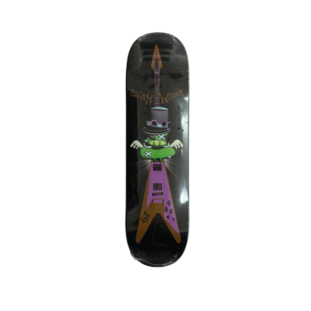 A skateboard deck with a black background and a graphic of a green character riding a purple and brown electric guitar, placed on a white surface.