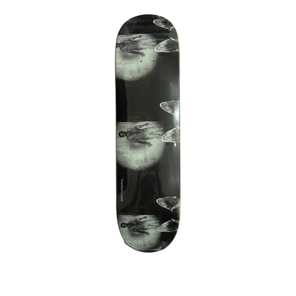 A skateboard deck with a black and white artistic print of a figure in a spotlight, displayed vertically on a white surface.